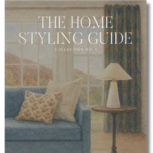 Könnte beinhalten: Das Cover eines Buches mit dem Titel „THE HOME STYLING GUIDE COLLECTION NO. 1“ zeigt ein blaues Sofa mit Kissen, einen Beistelltisch mit einer Lampe und ein Fenster. Das Kunstwerk verwendet eine gedämpfte Farbpalette, mit Fokus auf Inneneinrichtung.