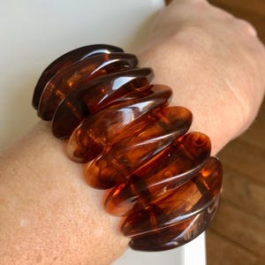 Puede incluir: Un brazalete de plástico marrón con un diseño ondulado único. El brazalete está hecho de varias piezas que están conectadas entre sí.