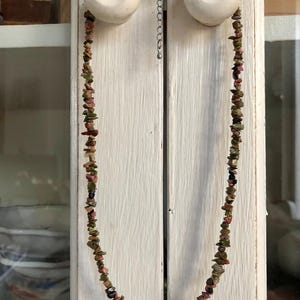 Peut inclure: Un collier composé de petites pierres brutes et irrégulières dans des tons vert olive, rose poudré et brun foncé. Le bijou est doté d'un fermoir mousqueton en métal argenté et d'une chaînette d'extension réglable avec une petite breloque ronde.