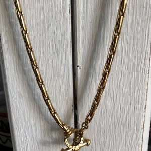 Peut inclure: Un collier à chaîne doré composé d'une série de maillons allongés et arrondis reliés en un motif continu. Le collier est fixé par un fermoir à bascule, constitué d'un anneau circulaire et d'une barre horizontale, tous deux en métal doré.