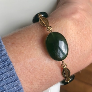 May include: A green stone bracelet with gold metal links. The bracelet has a large oval-shaped green stone in the center.