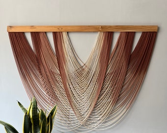 May include: A wall hanging made of woven yarn in shades of brown, beige, and white. The yarn is arranged in a symmetrical pattern, creating a modern and minimalist design.