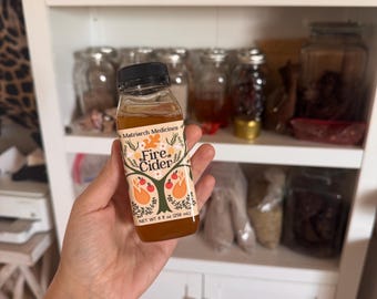 May include: A small glass bottle of Fire Cider with a black cap. The label features a tree design with red and orange accents. The bottle contains a brown liquid and is labeled "NET WT 8 fl oz (258 ml)."
