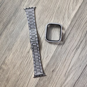 Puede incluir: Una correa de reloj de metal plateado y una funda protectora a juego, ambas totalmente incrustadas con peque&ntilde;as piedras claras y brillantes. La correa rectangular presenta un dise&ntilde;o de eslabones y la caja cuadrada tiene un borde interior negro.