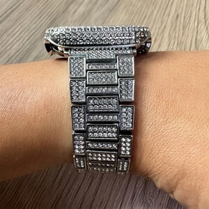 Puede incluir: Una caja de reloj plateada y una pulsera de eslabones a juego, ambas completamente incrustadas con numerosas piedras peque&ntilde;as, claras y brillantes. El reloj presenta una carcasa rectangular y un dise&ntilde;o de banda de m&uacute;ltiples eslabones, creando una apariencia uniforme y brillante.