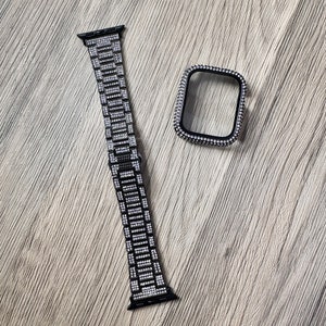 Puede incluir: Una correa de reloj inteligente negra y una funda protectora a juego, ambas con una incrustaci&oacute;n densa y uniforme de peque&ntilde;os cristales claros y brillantes en todas sus superficies visibles, creando un aspecto altamente reflectante y texturizado.