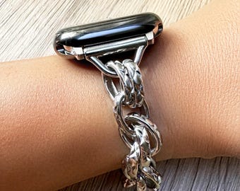 May include: A smartwatch with a glossy black screen and a silver-toned metal watch band. The band features a series of interlocking, thick, circular links with a textured, diamond-patterned surface that reflects light across the metallic finish.