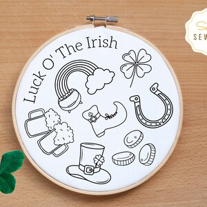May include: A white embroidery hoop with the text "Luck O' The Irish" and various Irish-themed illustrations, including a pot of gold, a four-leaf clover, a horseshoe, a leprechaun's hat, and a pint of beer.