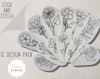 Könnte beinhalten: Ein Set aus 12 weißen Stoffformen mit schwarzen Linienzeichnungen verschiedener Blumen und Blätter. Die Formen sind fächerförmig angeordnet und der Text "STICK AND STITCH 12 DESIGN PACK" ist am unteren Rand des Bildes sichtbar.