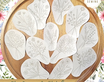 May include: Ten white fabric patches with different floral embroidery designs. The patches are arranged on a wooden tray. The text "Stick and Stitch" is printed on a brown banner below the tray.