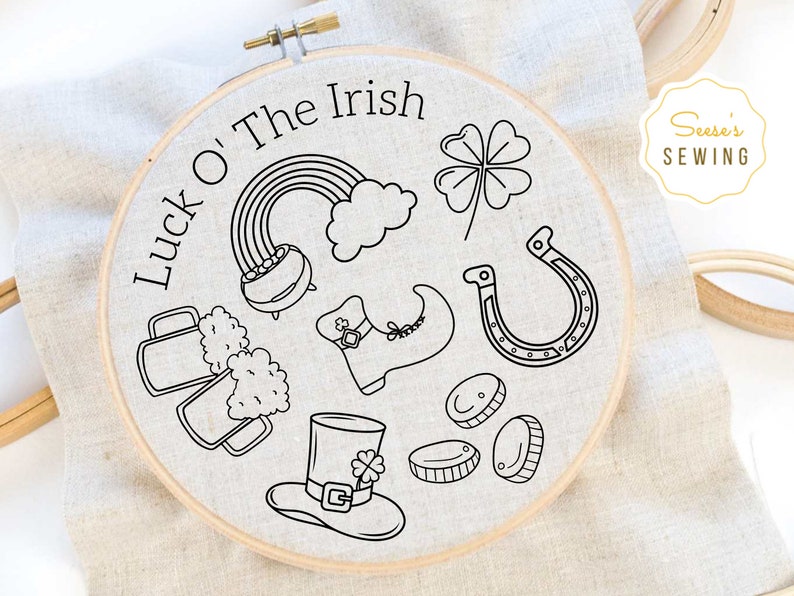 May include: A black and white embroidery hoop with the text "Luck O' The Irish" and various Irish symbols including a pot of gold, a rainbow, a four-leaf clover, a horseshoe, a beer mug, a leprechaun hat, and a shoe.