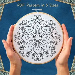 May include: A black and white mandala design on a white canvas in a wooden embroidery hoop. The design features a large flower with intricate details.