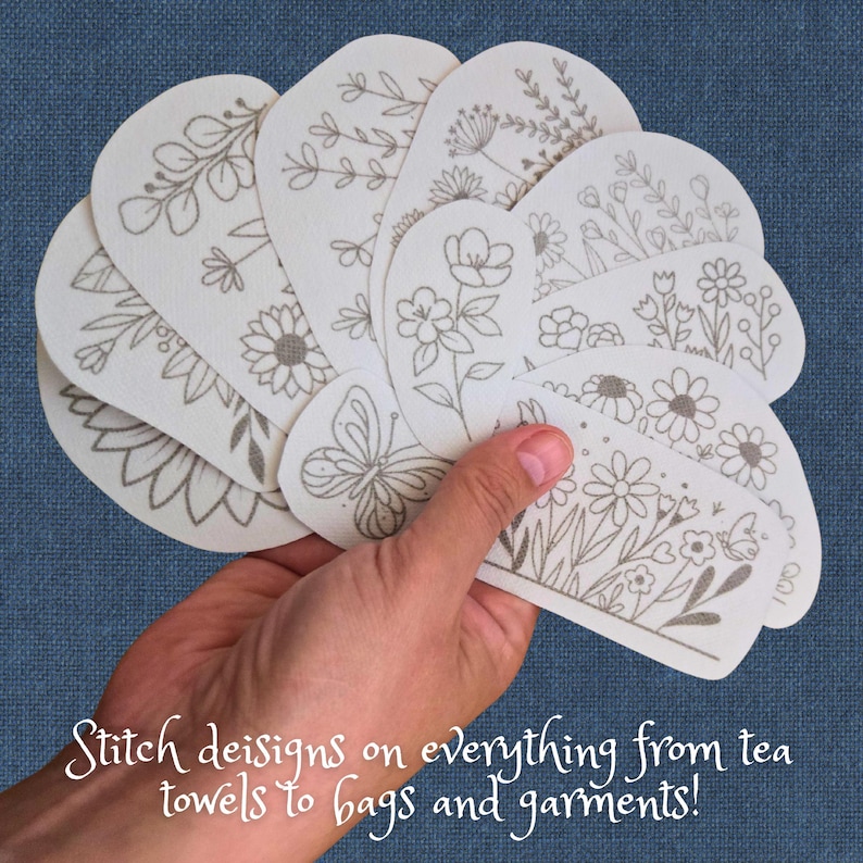 K&ouml;nnte beinhalten: Eine Hand h&auml;lt mehrere cremefarbene, ovale Stoffflicken mit gestickten Blumen- und Schmetterlingsmotiven. Die Flicken zeigen verschiedene botanische Illustrationen in Grau. Der Text unten lautet: "Stitch designs on everything from tea towels to bags and garments!"