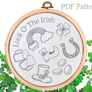 May include: A black and white embroidery pattern for a hoop art project. The design features Irish symbols such as a pot of gold, a rainbow, a horseshoe, a shamrock, a beer stein, a leprechaun's shoe, and a leprechaun's hat. The text "Luck o' The Irish" is written in a circle around the design.