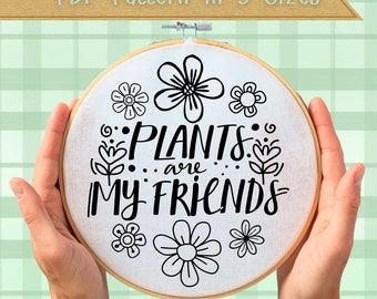 Puede incluir: Un aro de bordado blanco con bordado negro del texto "Plants are my friends" rodeado de pequeños diseños de flores.