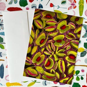 May include: A rectangular greeting card featuring a detailed illustration of numerous green Venus flytrap plants with red interiors and pink cilia, paired with a plain white envelope, resting on a surface patterned with colorful insects and feathers.