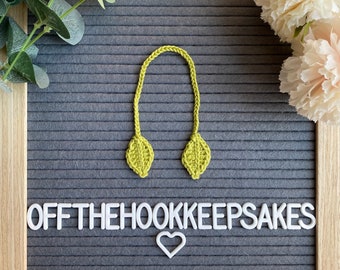 May include: A green crocheted leaf bookmark with the text "OFFTHEHOOKKEEPSAKES" and a white heart on a gray letter board.