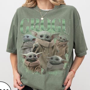 Pode incluir: Camiseta verde com a palavra "GROGU" em gradiente verde e um gr&aacute;fico de Grogu, tamb&eacute;m conhecido como Baby Yoda, de The Mandalorian. O design inclui v&aacute;rias imagens de Grogu.