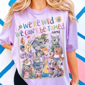 Puede incluir: Una camiseta de color lila claro con un gr&aacute;fico colorido de varios personajes de animales de dibujos animados. El texto "We're Wild, We Can't Be Tamed" se muestra encima de los personajes, con espacio para un nombre. El dise&ntilde;o incluye una placa de polic&iacute;a.