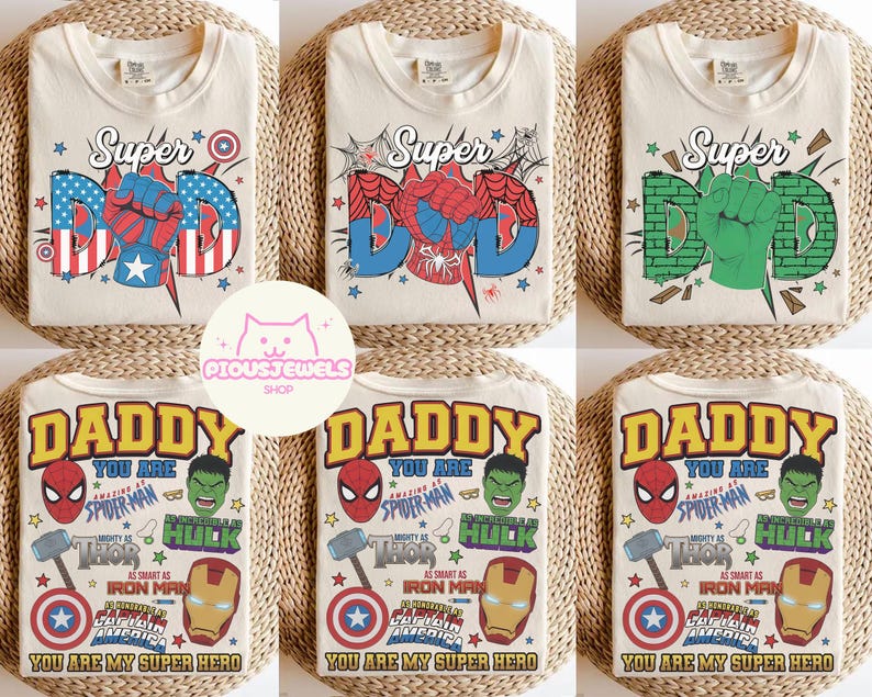 May include: A collection of six cream-colored t-shirts featuring graphic prints of superhero-themed designs. The top row displays the word Super with a fist replacing the letter O, while the bottom row features the text Daddy You Are My Super Hero.