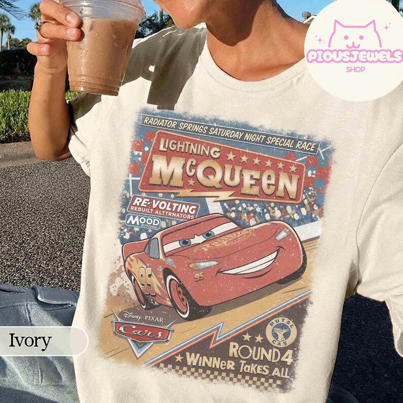 May include: Ivory-colored t-shirt featuring a graphic of Lightning McQueen from the Disney Pixar Cars movie. The design includes the text "Lightning McQueen" and "Radiator Springs Saturday Night Special Race". The shirt has a vintage, distressed look.