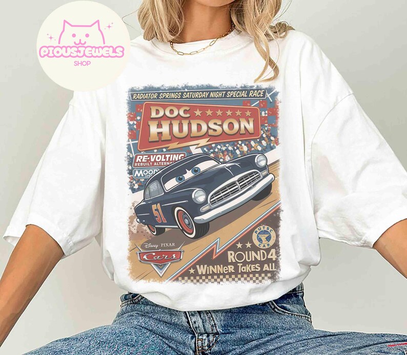 May include: White t-shirt featuring a graphic of Doc Hudson from the Disney Pixar Cars movie. The design includes the text "Radiator Springs Saturday Night Special Race" and "Winner Takes All". The car is dark blue with the number 51.