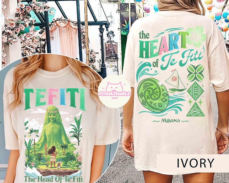 May include: Ivory-colored t-shirt featuring the text "TEFITI" in colorful letters. The front graphic depicts a green figure and the text "The Head Of Te Fiti". The back of the shirt has the text "The Heart of Te Fiti" and a Moana-themed design.