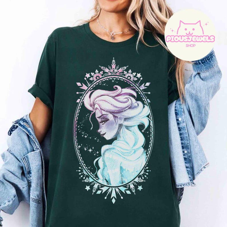 May include: Dark green t-shirt featuring a portrait of a woman with light blue and purple hair, framed in an oval with a decorative border. The design is reminiscent of a popular animated character. The shirt has short sleeves and a relaxed fit.