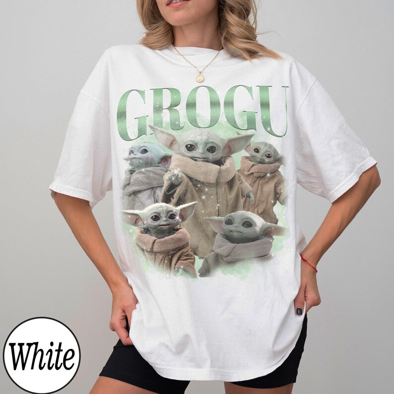 Pode incluir: Camiseta branca com um gr&aacute;fico de Grogu, tamb&eacute;m conhecido como Baby Yoda, de The Mandalorian. A palavra "GROGU" &eacute; impressa em verde acima da imagem de Grogu. A camiseta tem um corte folgado.