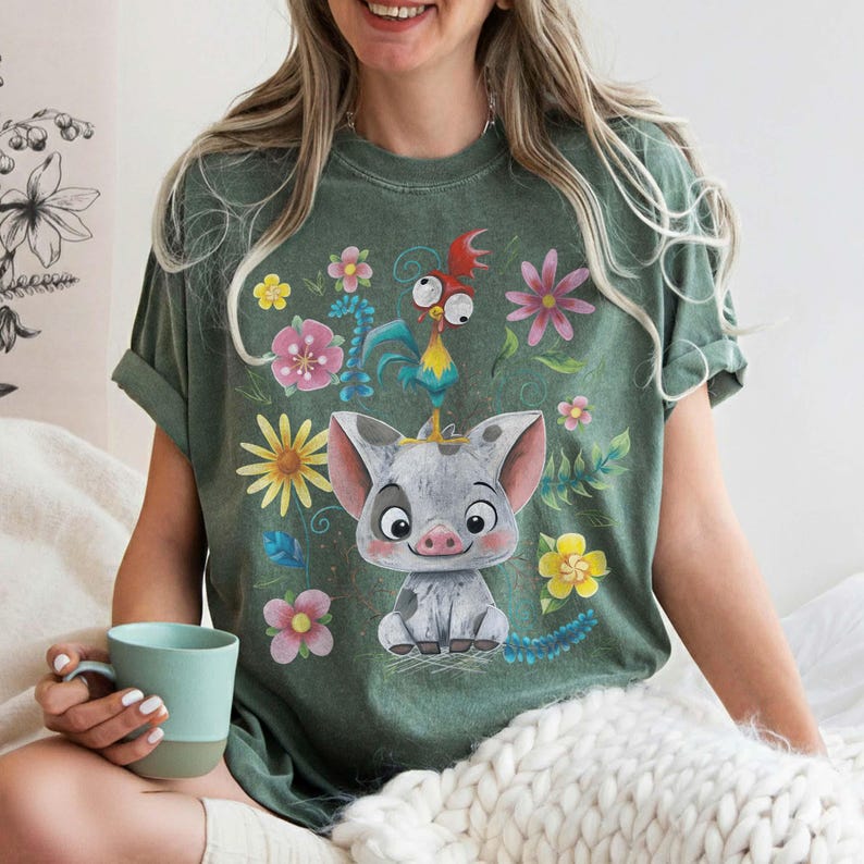Puede incluir: Camiseta verde con un cerdo de dibujos animados con una corona, rodeado de flores coloridas y un gallo. La camiseta tiene un corte relajado, ideal para el uso diario. El dise&ntilde;o es brillante y atractivo, para los fan&aacute;ticos de los personajes animados.