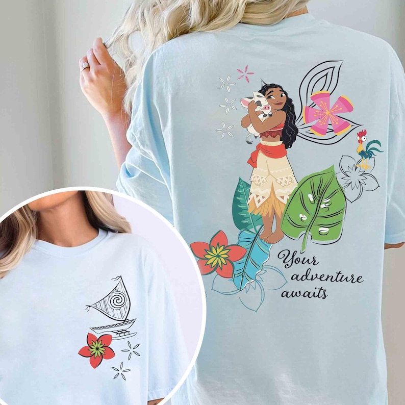 May include: Pale blue t-shirt with a Polynesian-themed graphic on the back, including a woman, pig, flowers, and leaves. The text reads "Your adventure awaits". The front has a smaller image of a boat and flowers.