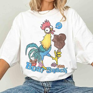 May include: White t-shirt with a colorful cartoon rooster holding a chocolate ice cream bar. The rooster has a red comb, yellow neck, and blue tail feathers. The text "Boat Snack" is printed in blue.