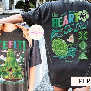 May include: Dark gray t-shirt featuring the text "TE FITI" and a graphic of a green goddess and a girl on an island. The back of the shirt displays the text "the HEART of Te Fiti" with ocean and floral designs. The word "MOANA" is also visible.