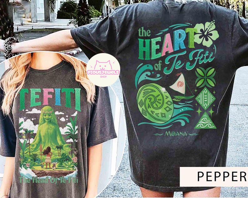 May include: Dark gray t-shirt featuring the text "TE FITI" and a graphic of a green goddess and a girl on an island. The back of the shirt displays the text "the HEART of Te Fiti" with ocean and floral designs. The word "MOANA" is also visible.