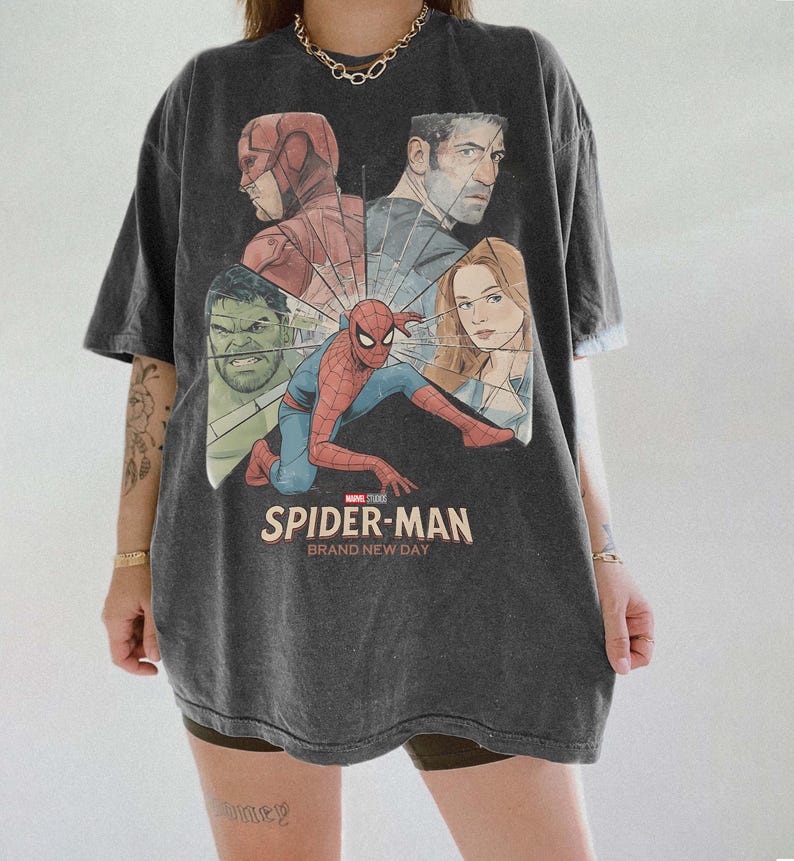 May include: Dark grey t-shirt with a graphic of Spider-Man and other Marvel characters. The text "SPIDER-MAN BRAND NEW DAY" is printed on the front. The shirt is short-sleeved and has an oversized fit.