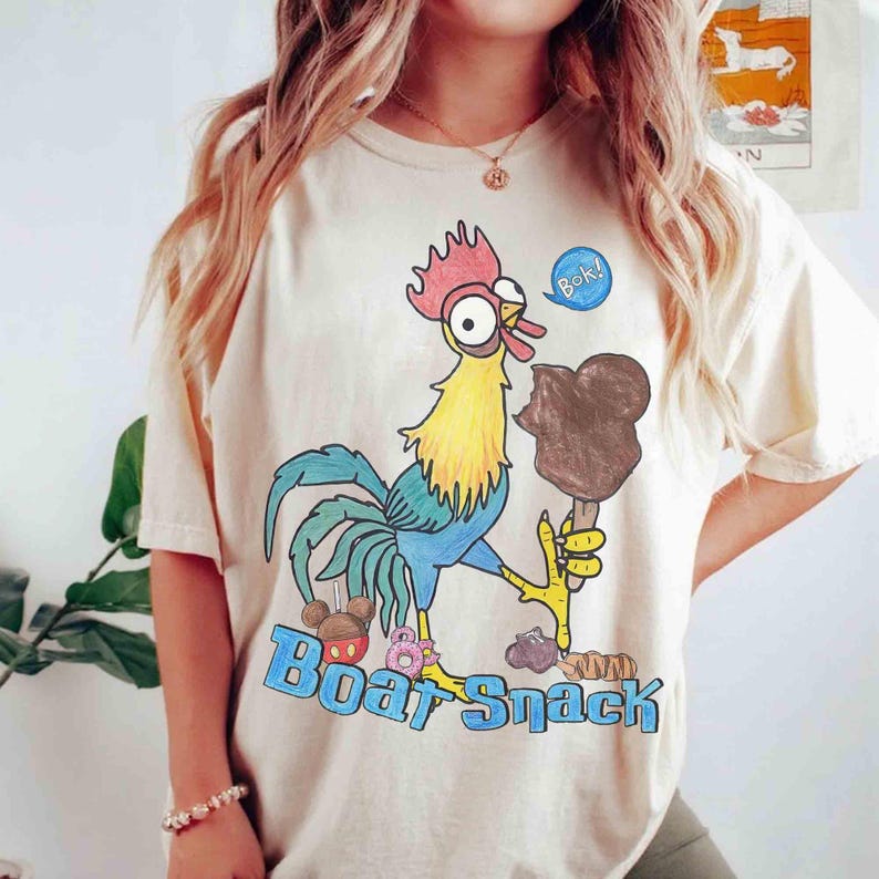 May include: Cream-colored t-shirt featuring a cartoon rooster holding a chocolate ice cream bar. The rooster has blue, yellow, and red coloring. The text "Boat Snack" is printed in blue below the rooster.