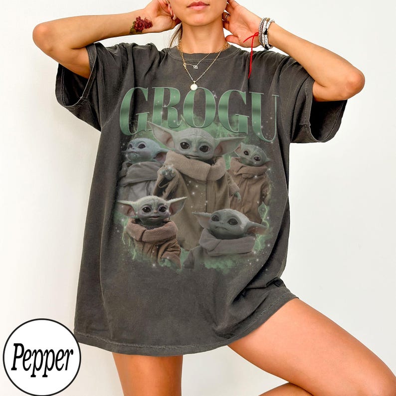 Pode incluir: Camiseta cinza escuro com a palavra "GROGU" em verde acima de um gr&aacute;fico de Grogu de The Mandalorian. O gr&aacute;fico mostra Grogu em v&aacute;rias poses. A camiseta tem mangas curtas e um corte folgado.
