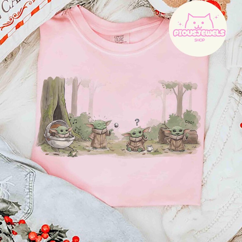 May include: A light pink t-shirt featuring a cartoon illustration of a character from a popular science fiction series. The design shows the character in various poses in a forest setting. The text "Cool!" is also included in the design.