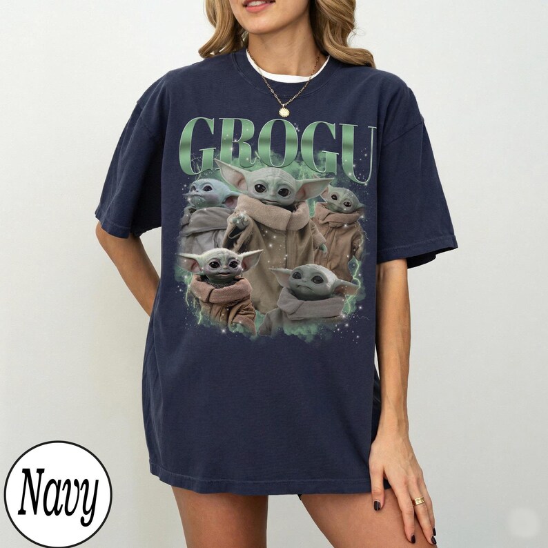 Pode incluir: Camiseta azul marinho com um gr&aacute;fico de Grogu, tamb&eacute;m conhecido como Baby Yoda, e a palavra "GROGU" em verde. O design inclui v&aacute;rias imagens de Grogu. A camiseta &eacute; um estilo confort&aacute;vel e casual.