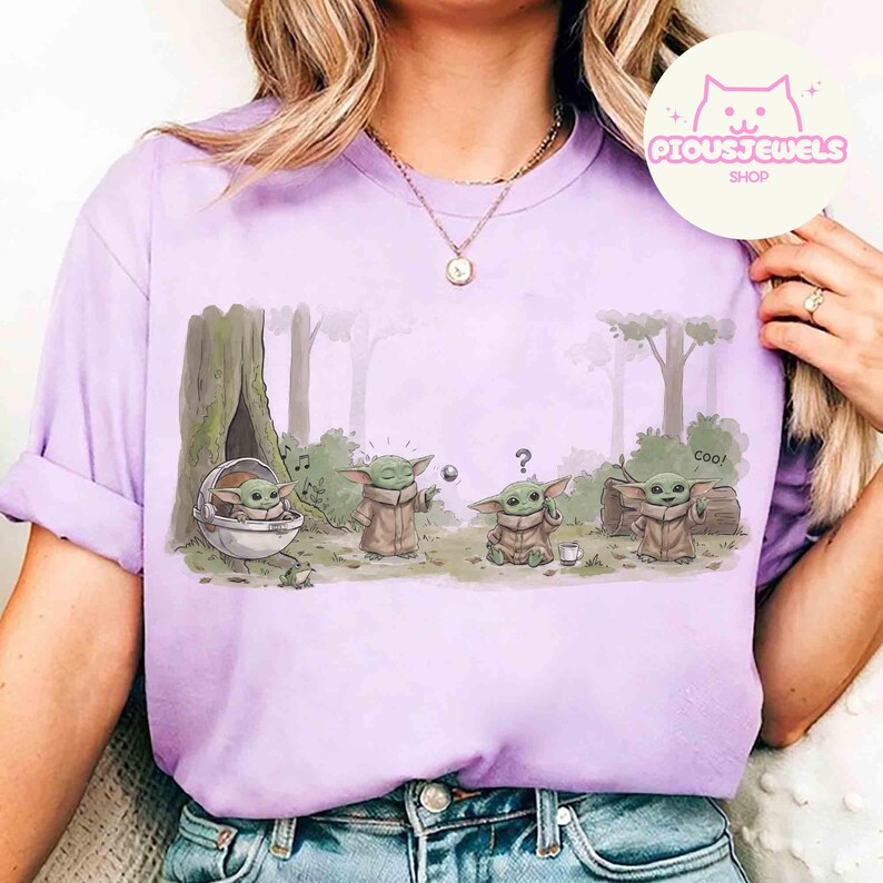 May include: A light purple t-shirt featuring a cartoon illustration of a character from a popular science fiction series. The graphic shows the character in various poses in a forest setting. The text "Coo!" is also visible.