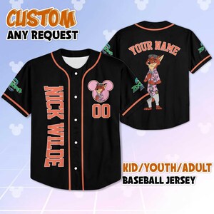 Puede incluir: Camiseta de b&eacute;isbol negra con ribete naranja y el texto "NICK WILDE" verticalmente en la parte delantera. Presenta un personaje de zorro de dibujos animados y el texto "YOUR NAME" en la espalda. La camiseta est&aacute; disponible en tallas para ni&ntilde;os, j&oacute;venes y adultos.