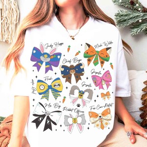 May include: White t-shirt featuring colorful bow tie designs with character names like "Judy Hopps" and "Nick Wilde." Each bow tie has unique details, including carrots and paw prints. The shirt has a casual, playful aesthetic.