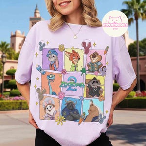 May include: A light purple t-shirt featuring a colorful graphic of characters from the animated movie "Zootopia 2". The design includes Judy Hopps, Nick Wilde, and other characters in a grid pattern. The text "Zootopia 2" is also visible.