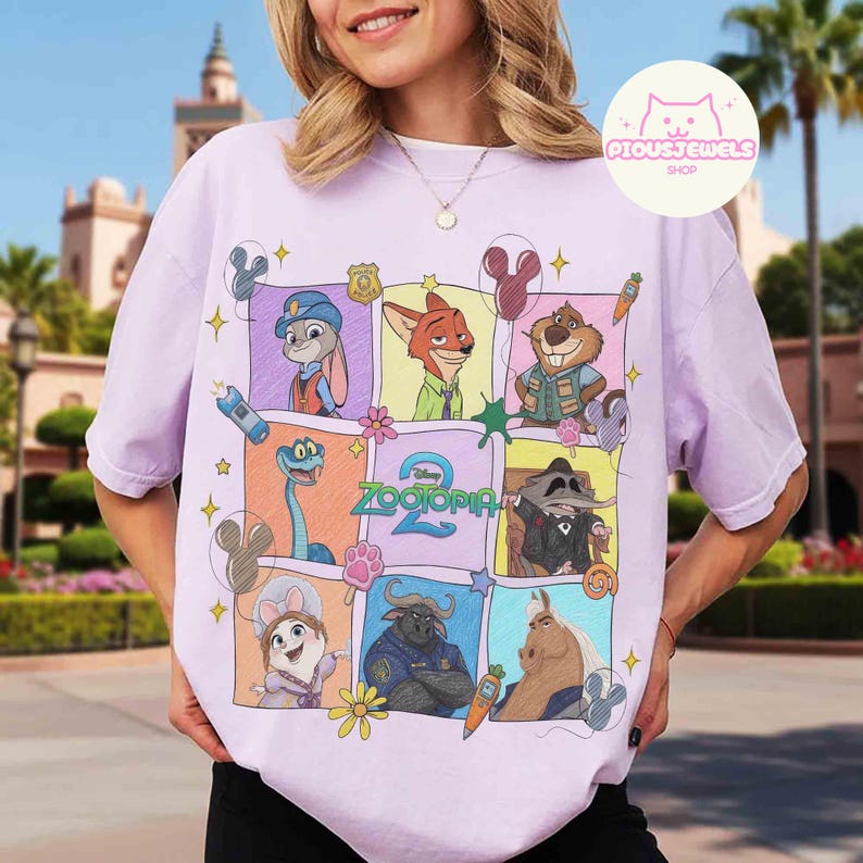May include: A light purple t-shirt featuring a colorful graphic of characters from the animated movie "Zootopia 2". The design includes Judy Hopps, Nick Wilde, and other characters in a grid pattern. The text "Zootopia 2" is also visible.