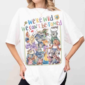 Puede incluir: Camiseta blanca con un gr&aacute;fico colorido de varios personajes de dibujos animados y el texto "We're Wild We Can't Be Tamed". El dise&ntilde;o incluye una insignia y un espacio para un nombre, en un estilo divertido.