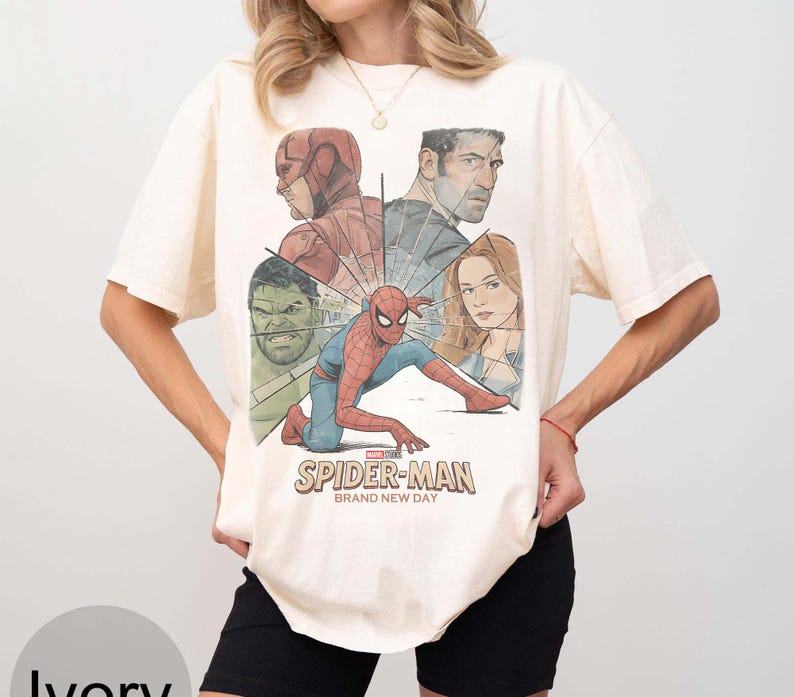 May include: Ivory t-shirt with a graphic of Spider-Man and other Marvel characters. The design includes the text "Spider-Man Brand New Day". The shirt has short sleeves and a crew neck.