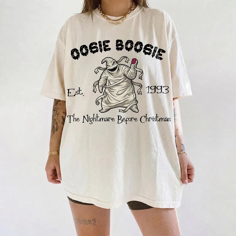 K&ouml;nnte beinhalten: Cremefarbenes T-Shirt mit dem Text "Oogie Boogie" &uuml;ber einer Illustration der Figur aus "The Nightmare Before Christmas". Die Grafik enth&auml;lt den Text "Est. 1993" und "The Nightmare Before Christmas."