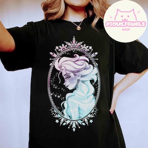 May include: Black t-shirt featuring a watercolor illustration of a woman with flowing blue and purple hair, framed by a decorative oval. The design includes stars and snowflake accents. The shop logo "PIOUSJEWELS SHOP" is in the upper right corner.