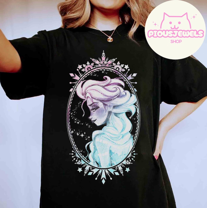 May include: Black t-shirt featuring a watercolor illustration of a woman with flowing blue and purple hair, framed by a decorative oval. The design includes stars and snowflake accents. The shop logo "PIOUSJEWELS SHOP" is in the upper right corner.