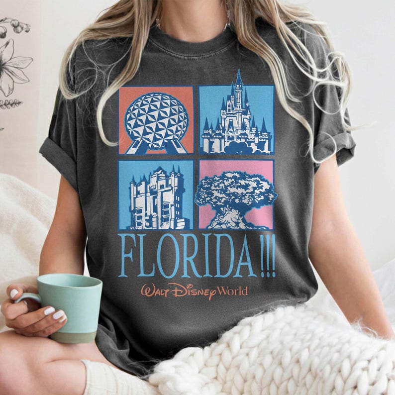 May include: Dark gray t-shirt featuring a colorful graphic of Florida landmarks, including a sphere, castle, and tree. The word "FLORIDA!!!" is printed below the images, with "Walt Disney World" underneath.